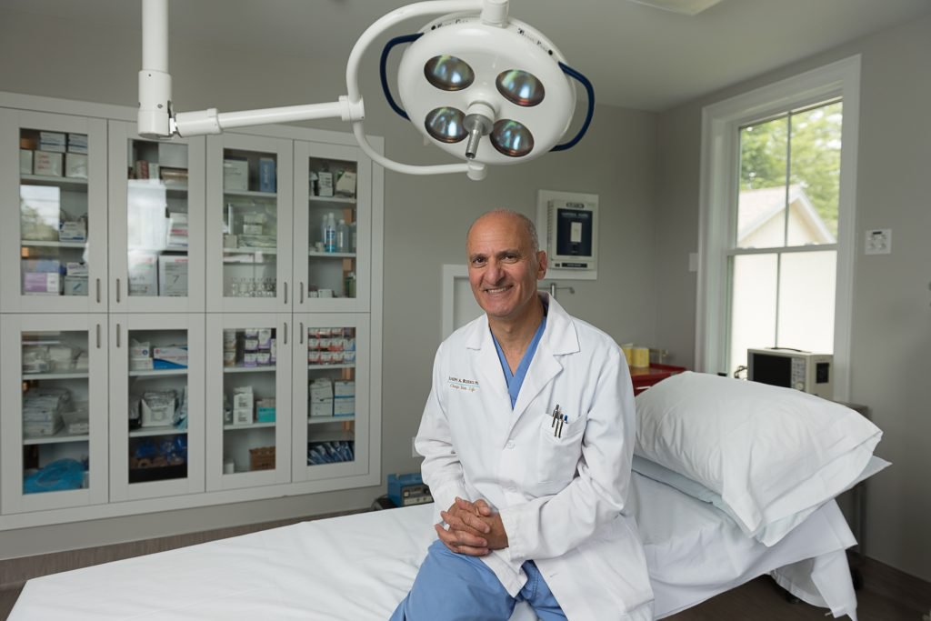 Dr. Russo - Boston plastic surgeon sitting on side of medical bed.